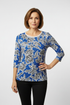 Mature model wearing blue paisley print top with white neckline trim